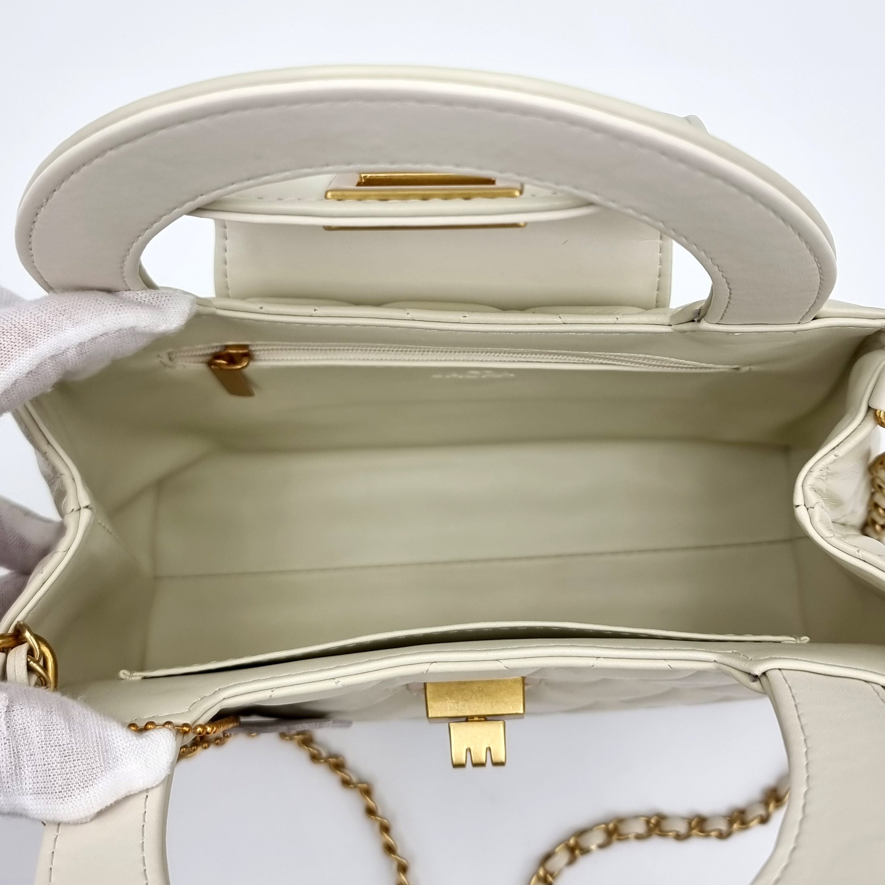 Close-up of a beige real leather handbag with gold accents on a light background
